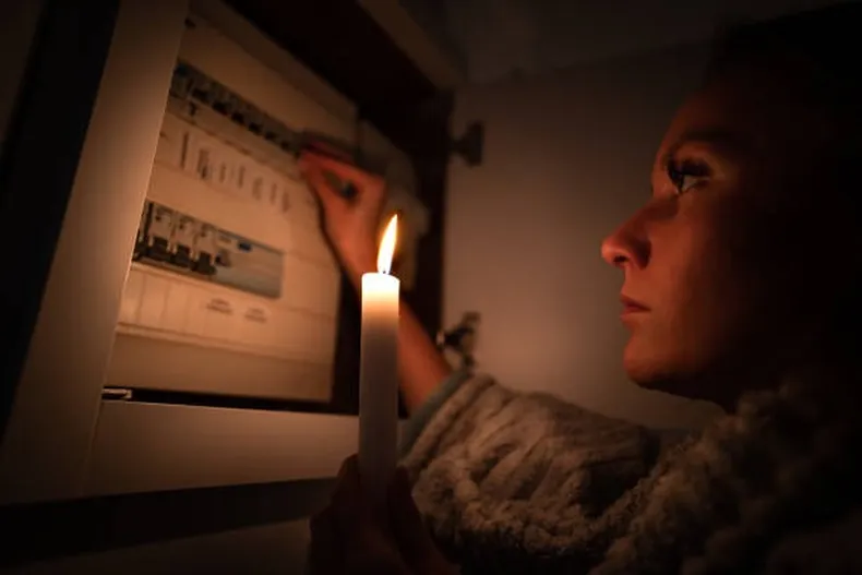 Fotografía de referencia de una mujer frente a un tablero eléctrico, iluminada por una vela.