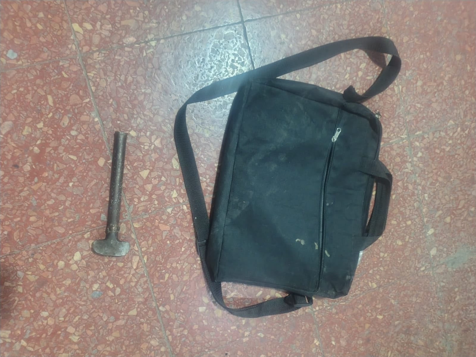 Morral negro y elemento metálico tipo martillo sobre un piso de baldosas, fotografiados en el procedimiento por el intento de robo a un comercio.