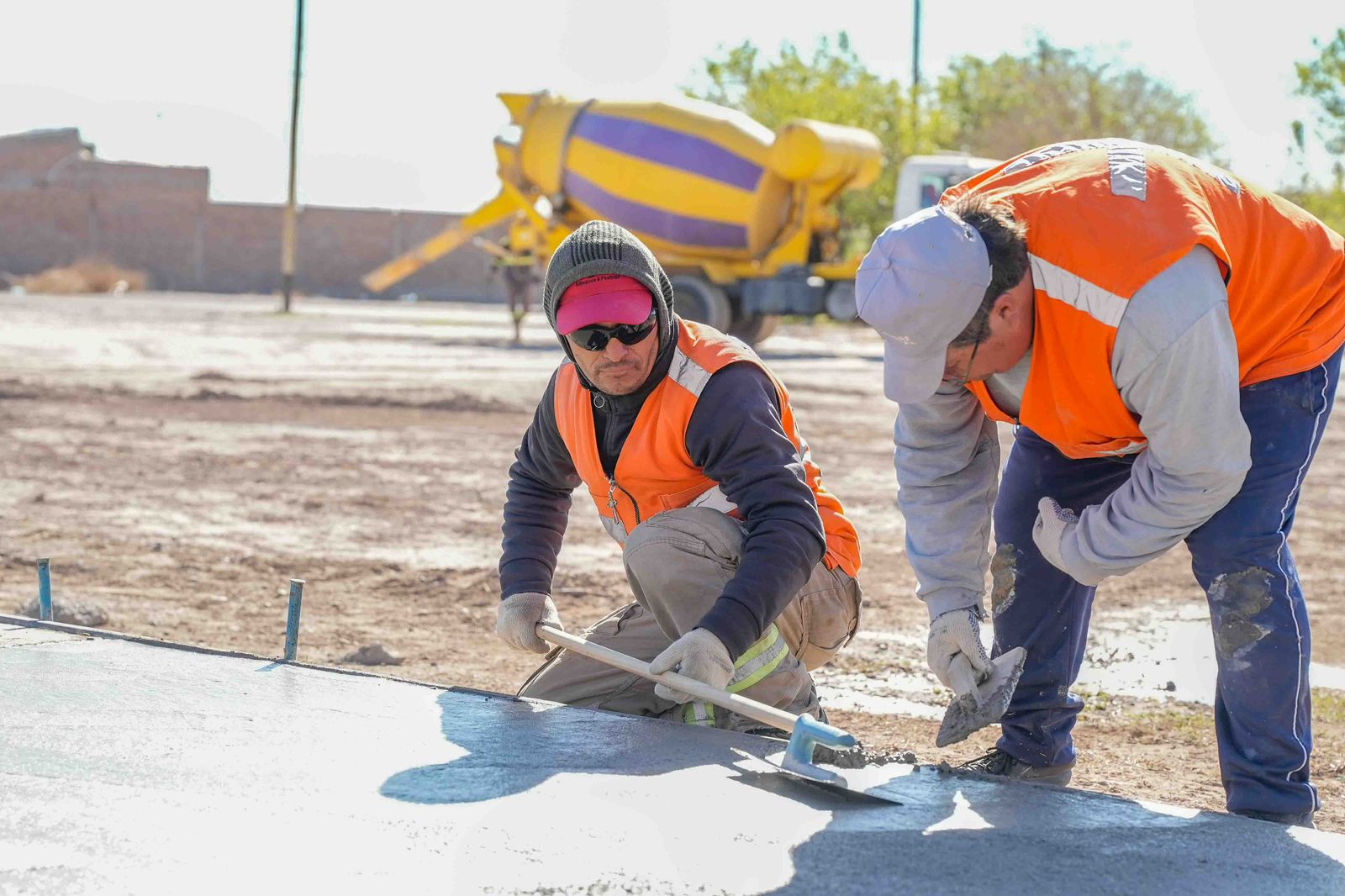 Dos trabajadores alisan el hormigón de una vereda durante la construcción de la nueva plaza del Loteo Santa Isabel.