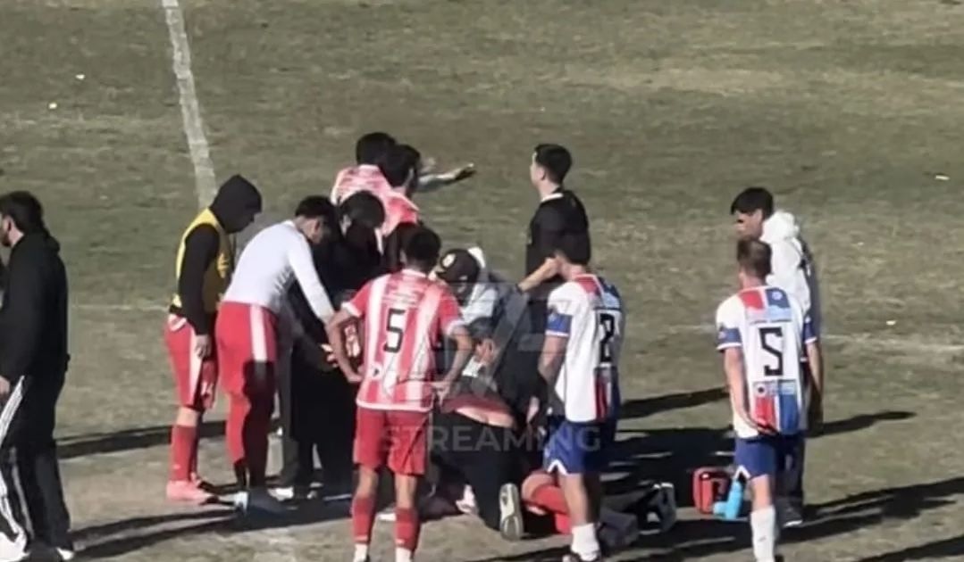 Jugadores y asistentes reunidos alrededor de un futbolista en el campo de juego. Imagen difundida por Del Sur Diario.