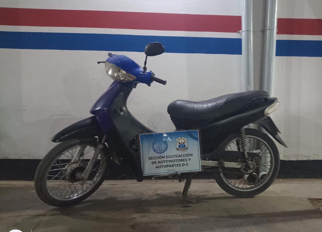 Motocicleta azul fotografiada junto al cartel de la Sección Sustracción de Automotores y Autopartes D-5.