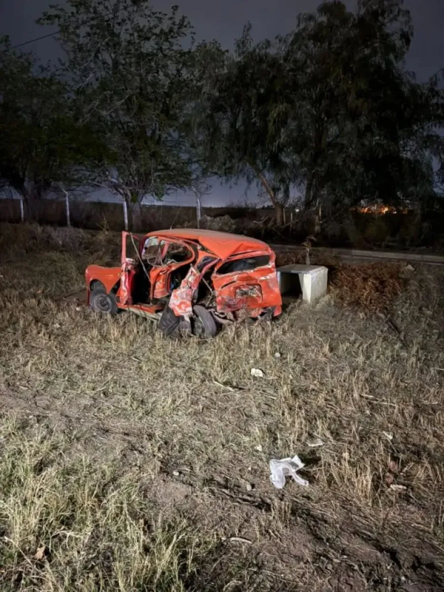 Automóvil rojo con graves daños fuera de la calzada, fotografiado de noche tras el siniestro.