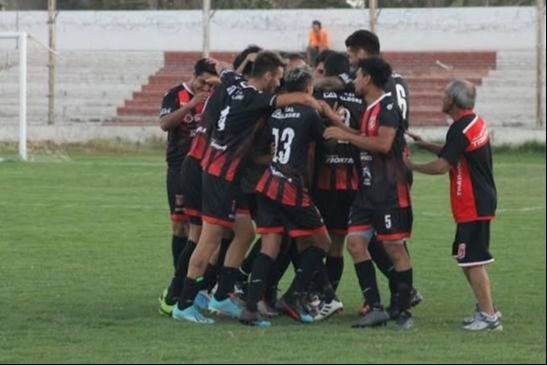 Jugadores de fútbol con camisetas rojas y negras se abrazan en una cancha.
