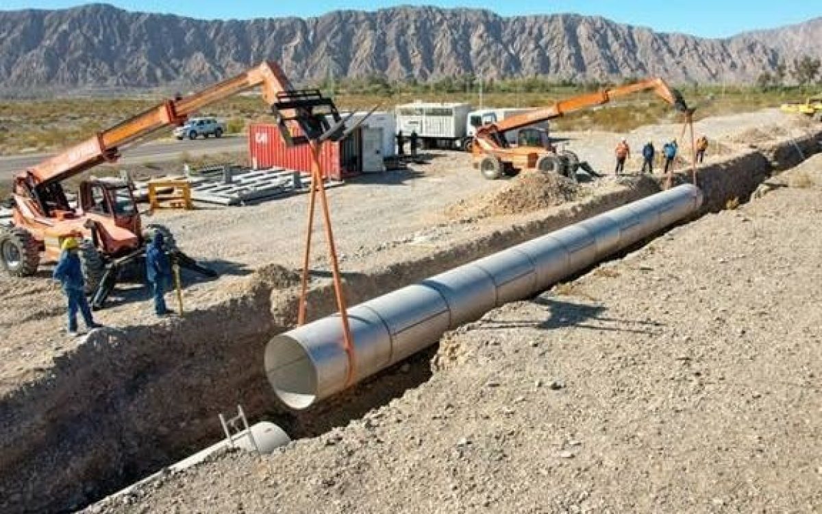Trabajadores y maquinaria colocan una cañería en una zanja durante una obra de acueducto.