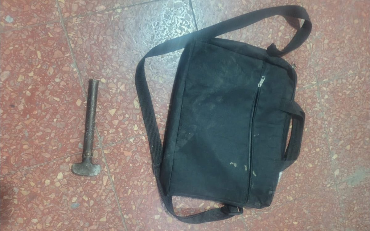 Morral negro y elemento metálico tipo martillo sobre un piso de baldosas, fotografiados en el procedimiento por el intento de robo a un comercio.