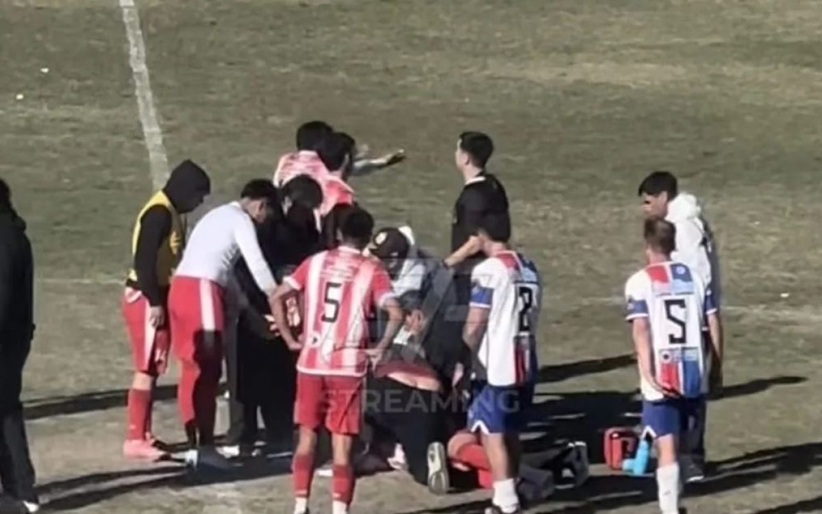 Jugadores y asistentes reunidos alrededor de un futbolista en el campo de juego. Imagen difundida por Del Sur Diario.