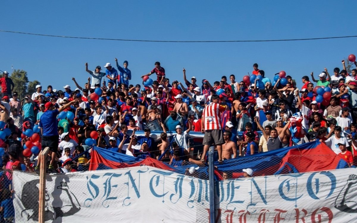 Hinchas de Villa Obrera en una tribuna con banderas rojas y azules