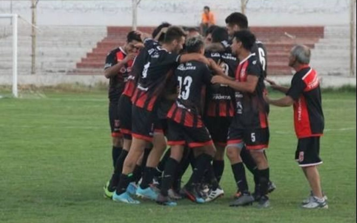 Jugadores de fútbol con camisetas rojas y negras se abrazan en una cancha.