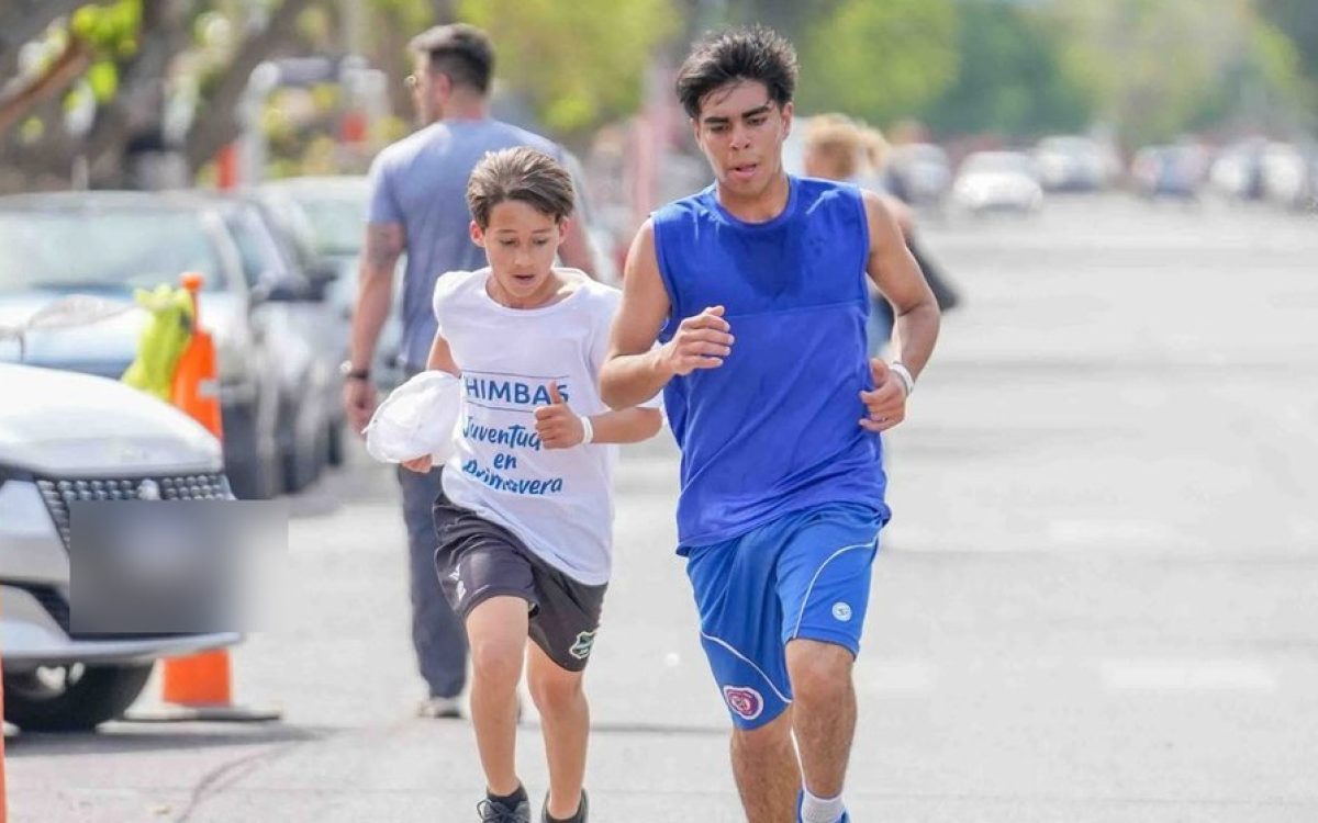Personas corriendo en una actividad deportiva al aire libre en Chimbas, con conos naranjas sobre la calle.