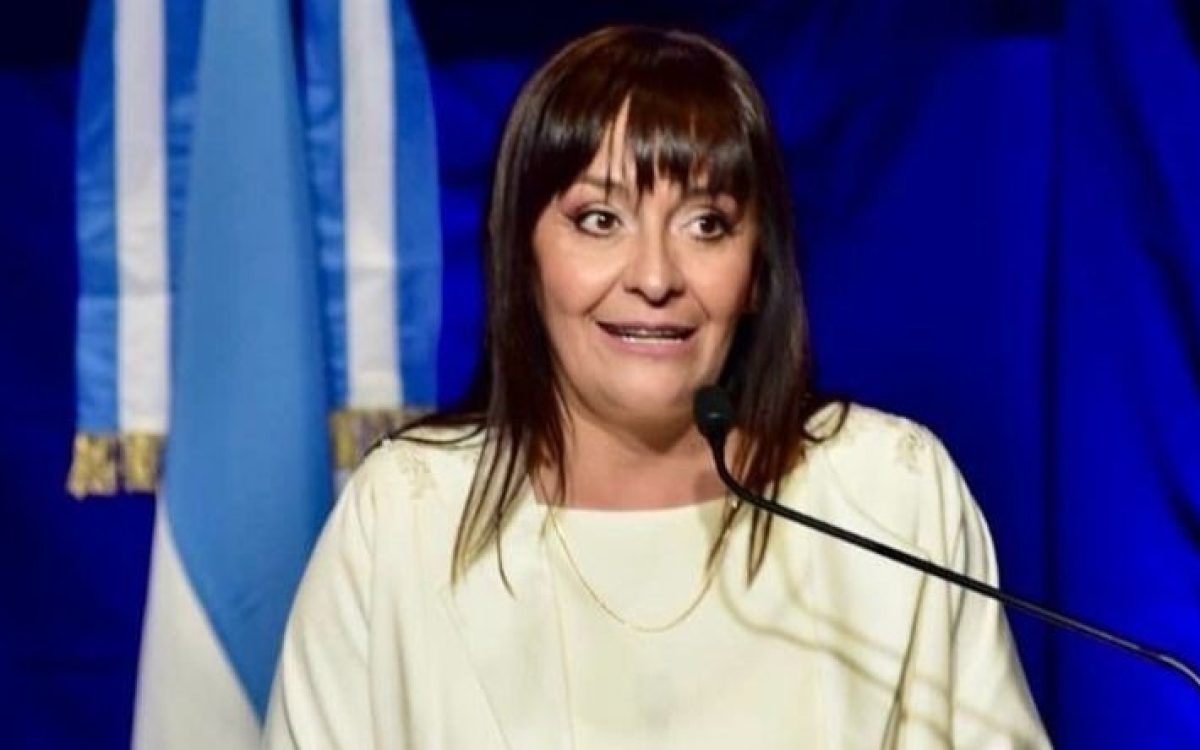 Daniela Rodríguez, intendenta de Chimbas, habla ante un micrófono con la bandera argentina de fondo