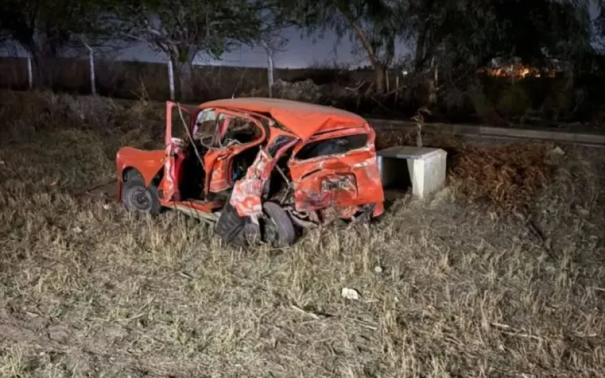 Automóvil rojo con graves daños fuera de la calzada, fotografiado de noche tras el siniestro.
