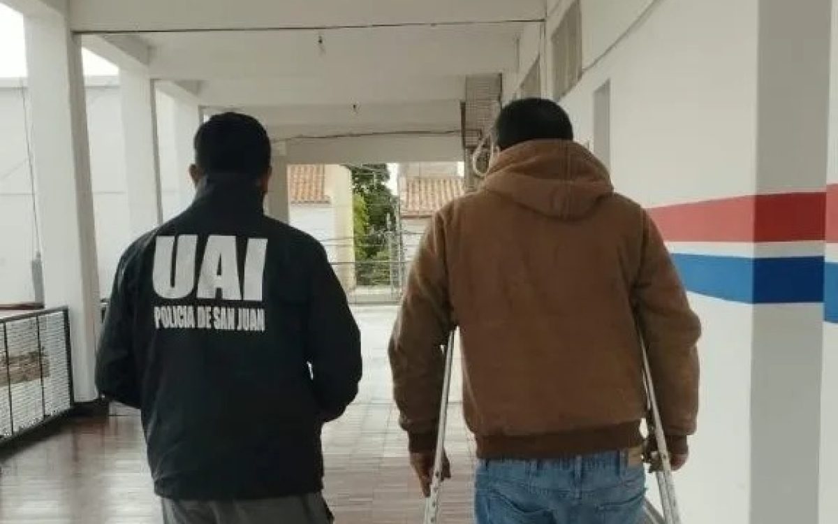 Efectivo de la UAI, de espaldas, camina junto a un hombre con muletas por un pasillo